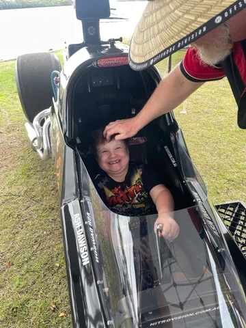 Young child smiling in the NitroVision dragster cockpit at a community event